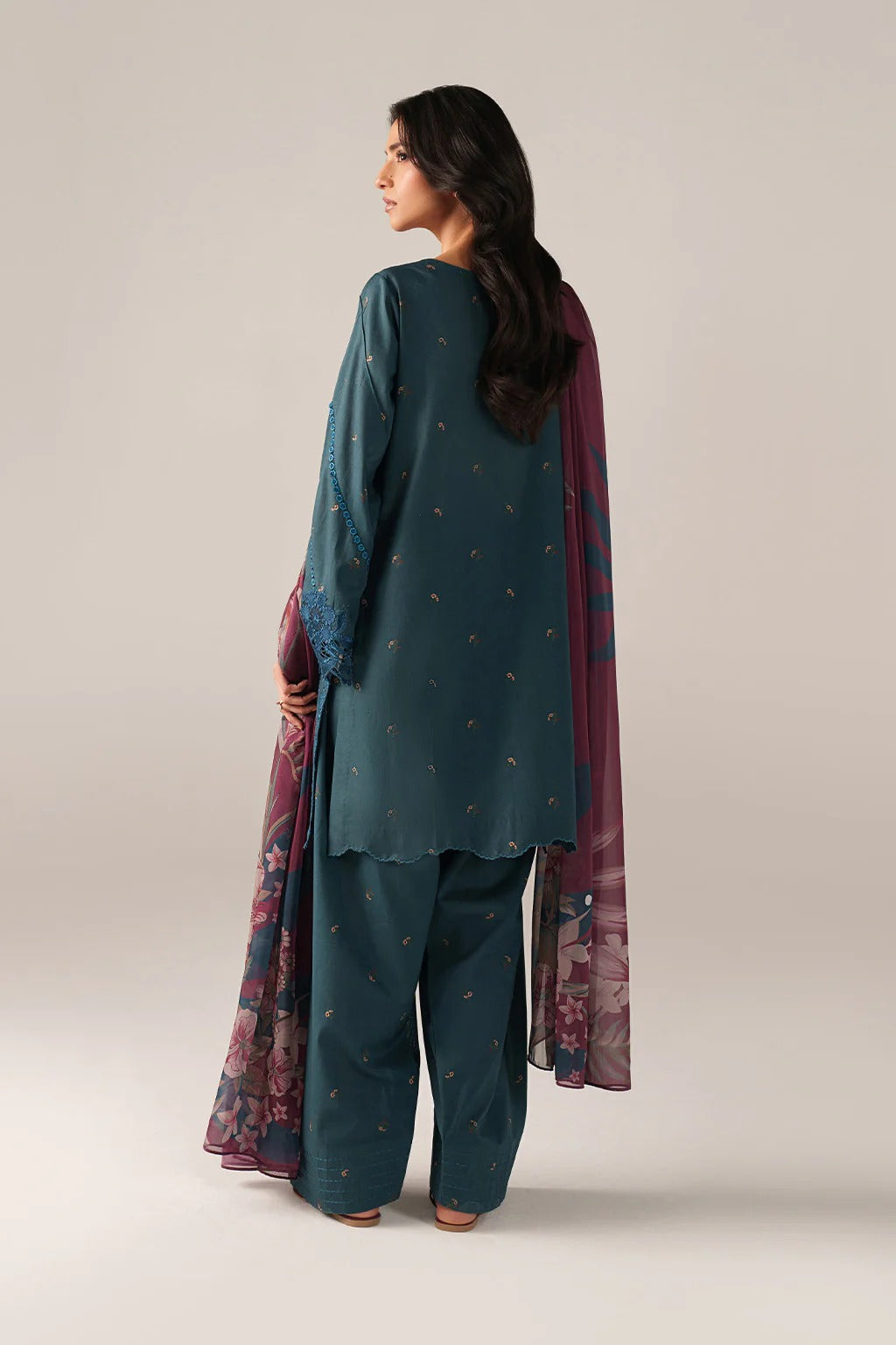 Woman wearing a teal traditional outfit with a floral dupatta on a plain background