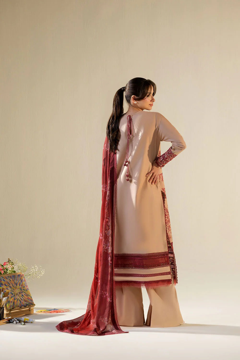Woman wearing a traditional outfit with a red and beige dupatta on a neutral background