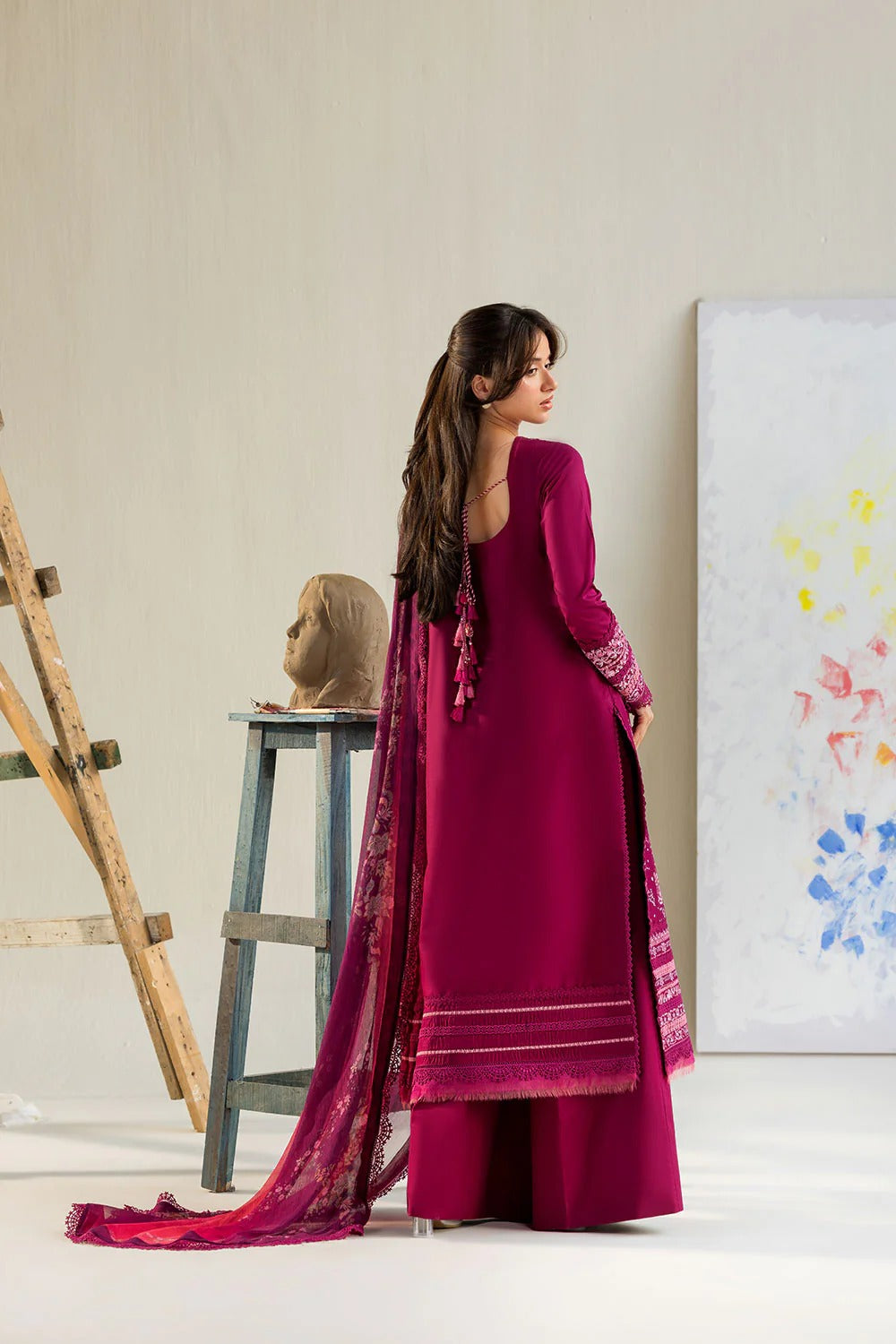 Woman in a magenta traditional outfit standing in a minimalistic room with a painting on the wall.