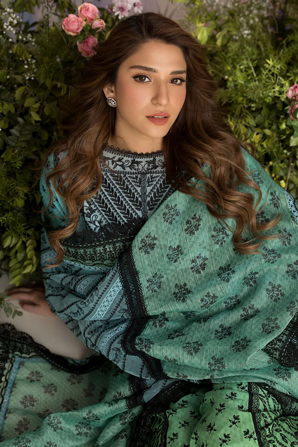 Woman wearing a green patterned outfit with floral decorations in a natural setting
