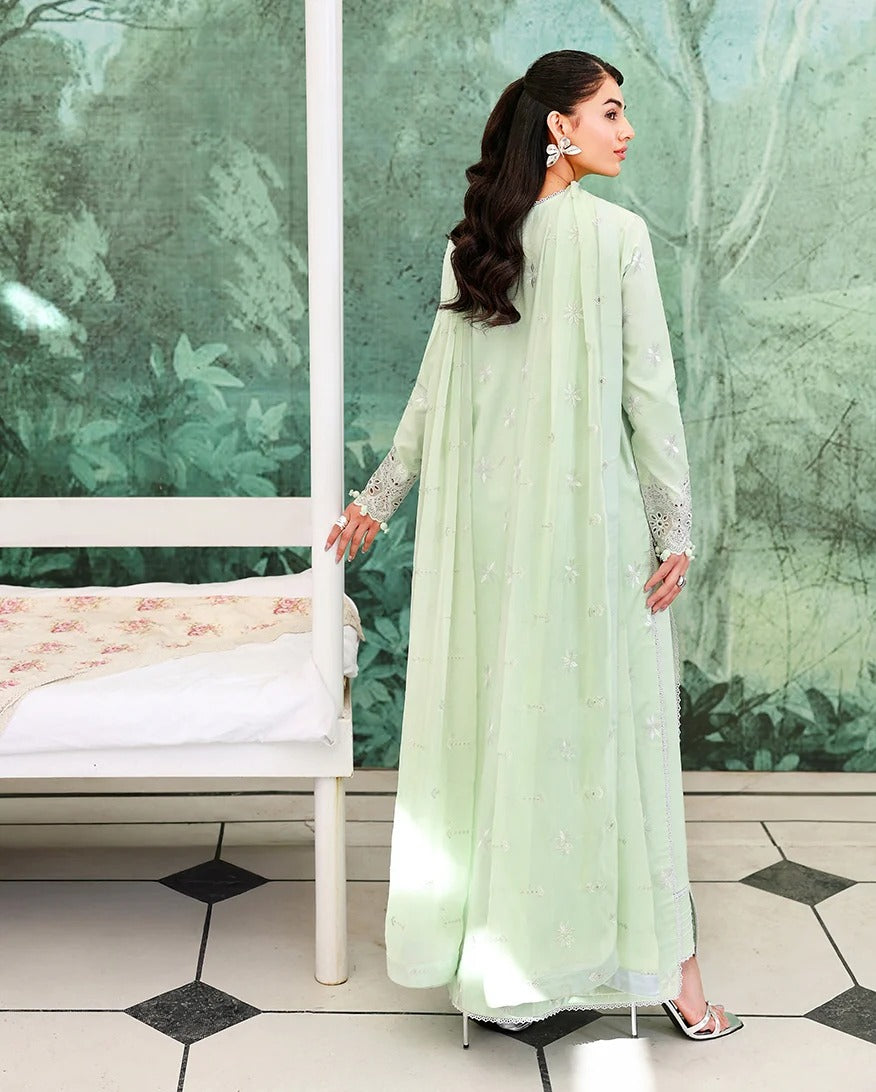 Woman in a light green traditional outfit standing in a room with a white bench and green wall.