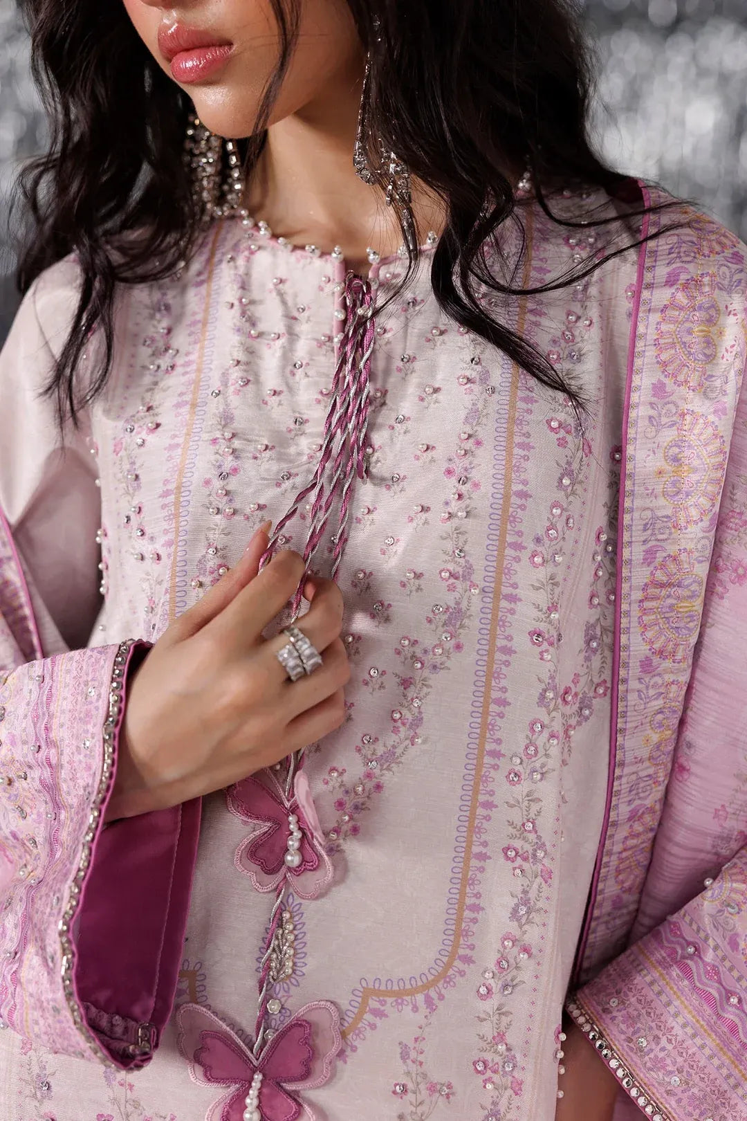 A close-up of a model wearing a light pink embroidered traditional outfit with pink and purple accents, featuring intricate floral embroidery, a sheer inner layer, and a matching patterned dupatta.