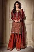 A woman models a traditional South Asian salwar kameez suit. The outfit features a deep maroon-red embroidered kurta with gold and silver metallic detailing, paired with matching wide-leg trousers in a rust-orange shade and a sheer dupatta.