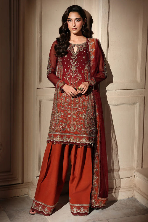 A woman models a traditional South Asian salwar kameez suit. The outfit features a deep maroon-red embroidered kurta with gold and silver metallic detailing, paired with matching wide-leg trousers in a rust-orange shade and a sheer dupatta.