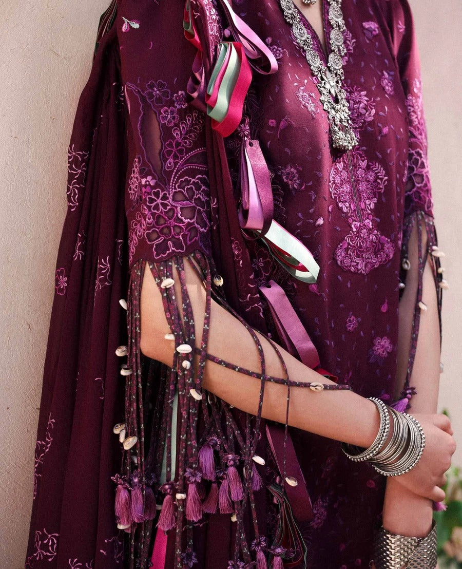 Purple embroidered garment with tassels and jewelry against a neutral background