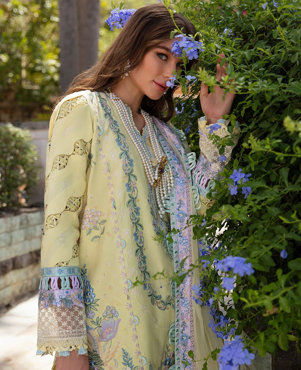 Woman in a light yellow embroidered dress standing among flowers and greenery