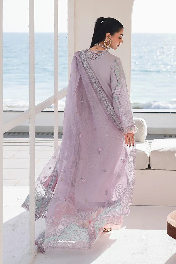 Woman in a light purple traditional outfit with silver embroidery standing by a window with a view of the ocean.