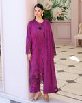 Woman in a purple embroidered outfit standing in a decorated room with floral decorations.