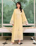 Woman in a light yellow embroidered outfit standing in front of a decorative green wall.