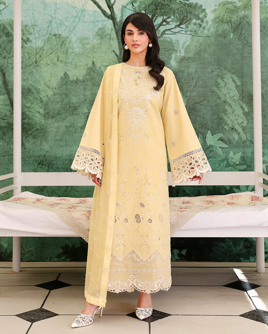 Woman in a light yellow embroidered outfit standing in front of a decorative green wall.