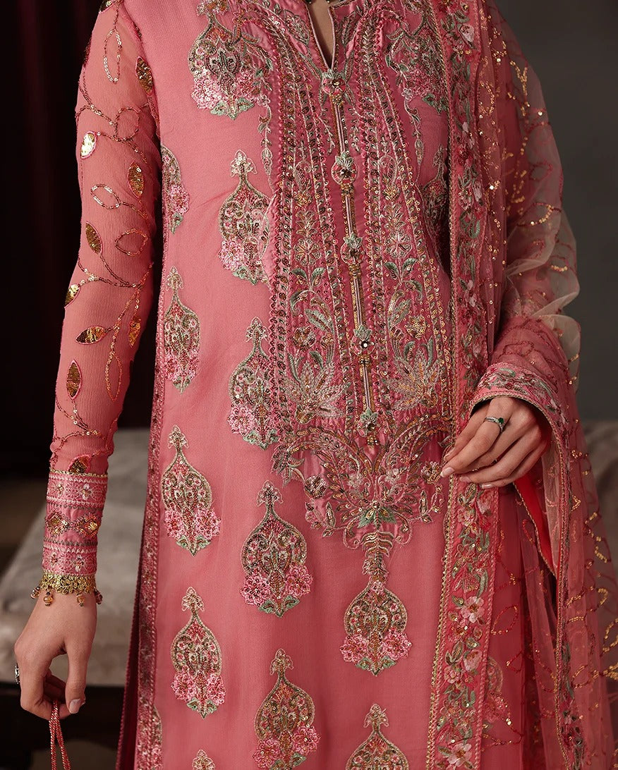 A close-up of a pink traditional embroidered outfit with ornate metallic and floral detailing, shown on a model against a dark indoor background.