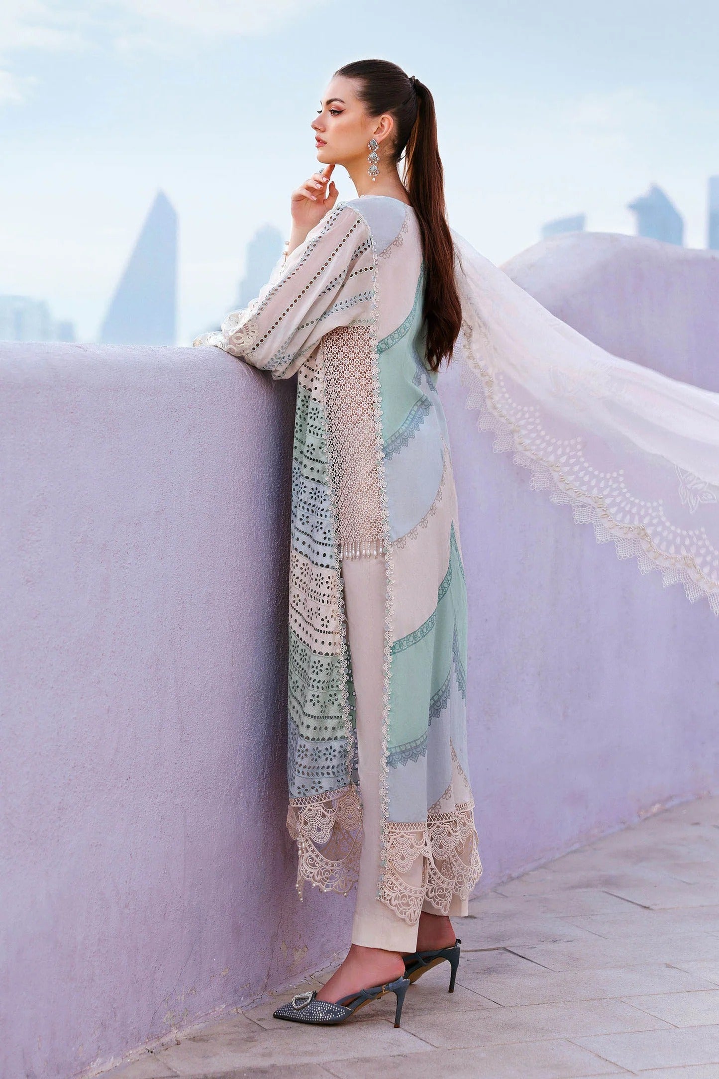 Woman in a long, patterned dress standing on a rooftop with city skyline in the background