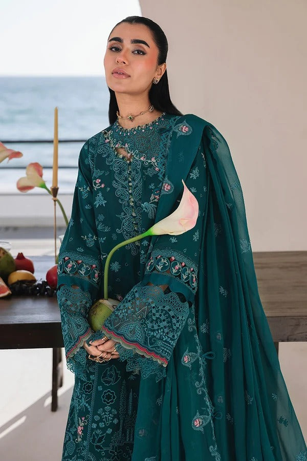 Woman in a teal embroidered outfit holding a pink flower indoors.