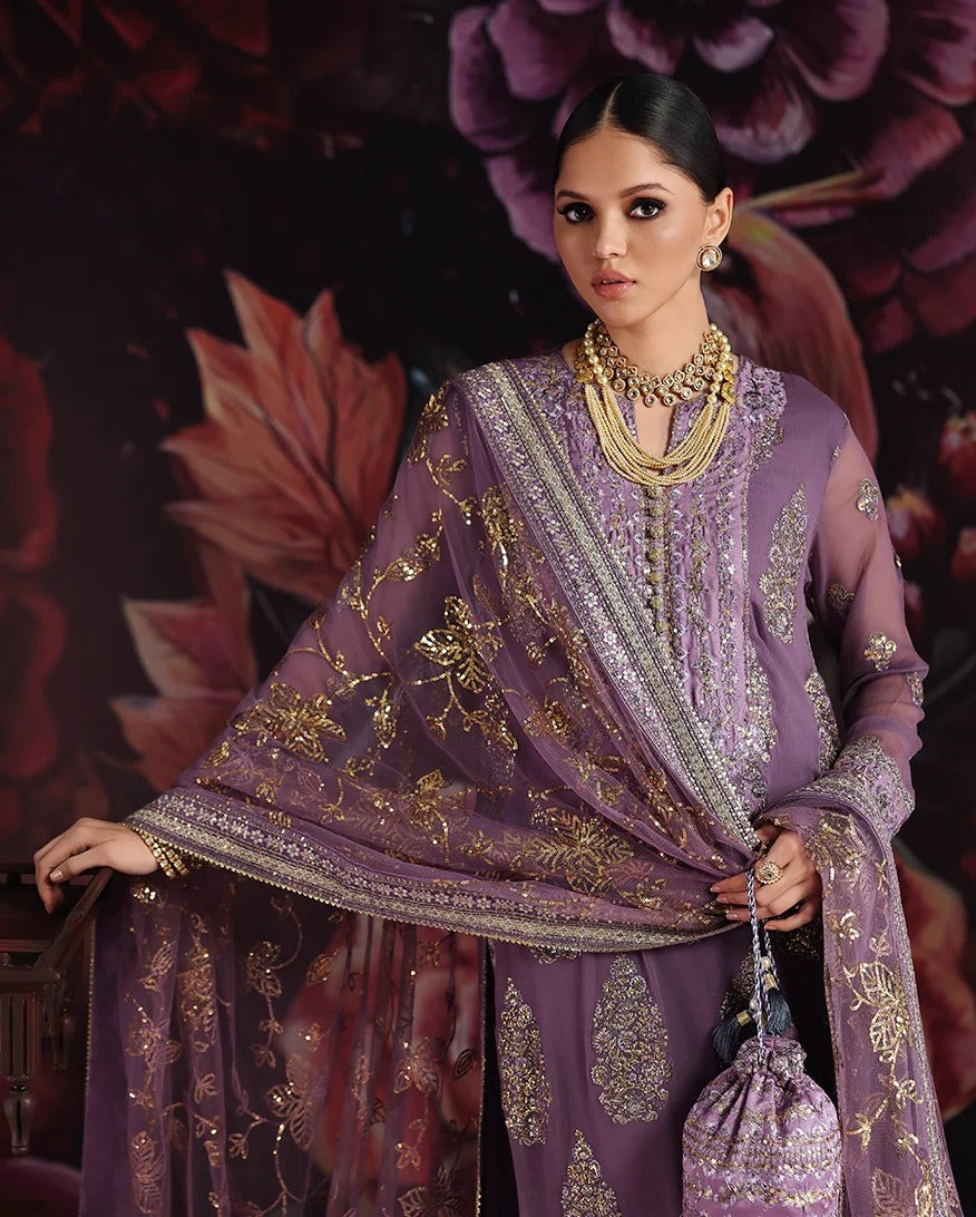 A woman models a purple embroidered traditional outfit with a matching sheer dupatta and gold embellishments, posed against a dark floral backdrop.