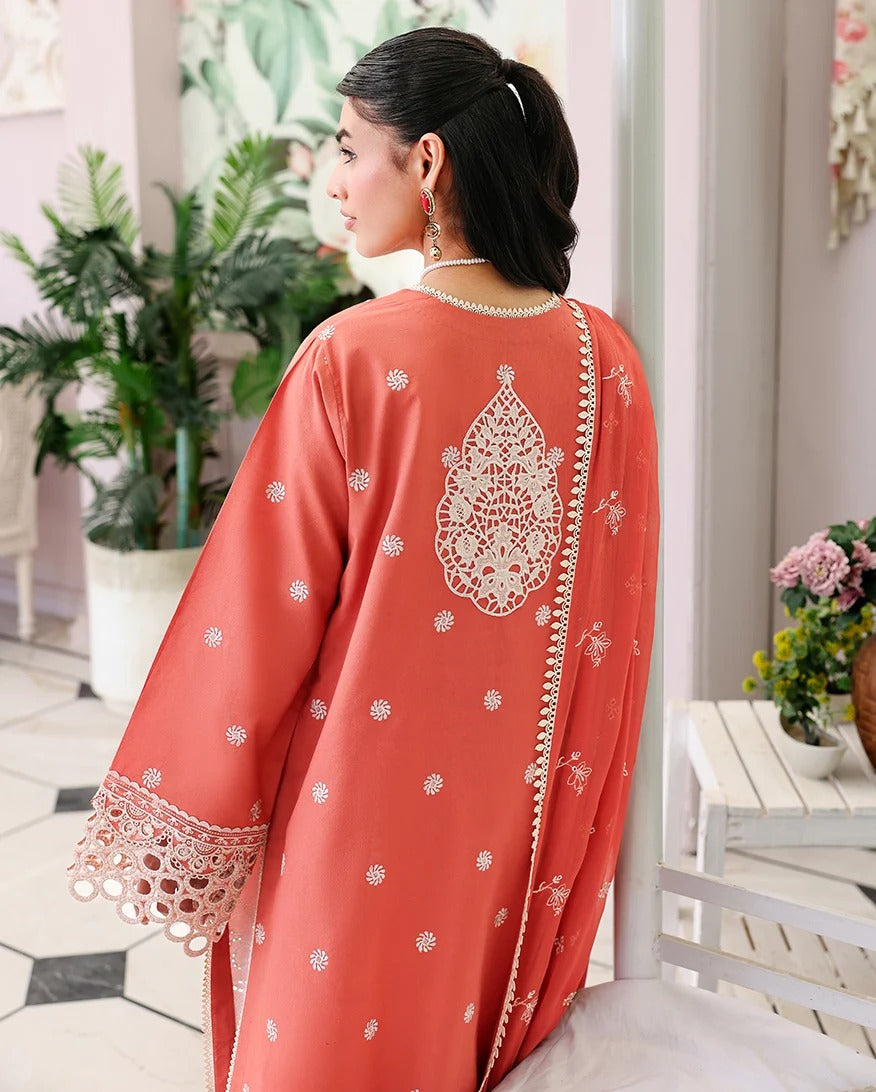 Woman wearing a coral pink traditional outfit with intricate white embroidery in an indoor setting.