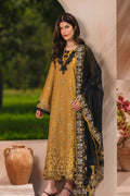 A woman models a traditional three-piece salwar kameez suit. The kurta is mustard yellow with black and gold floral embroidery, paired with a black dupatta featuring gold and silver zari borders and embroidery.