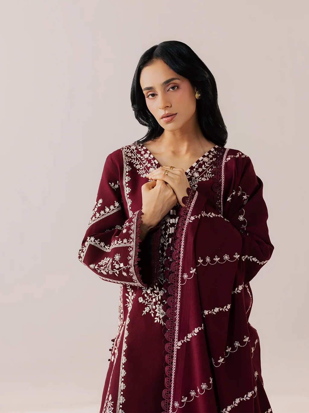 A woman wearing a long-sleeved maroon embroidered tunic with white floral patterns, posed against a solid light beige background.