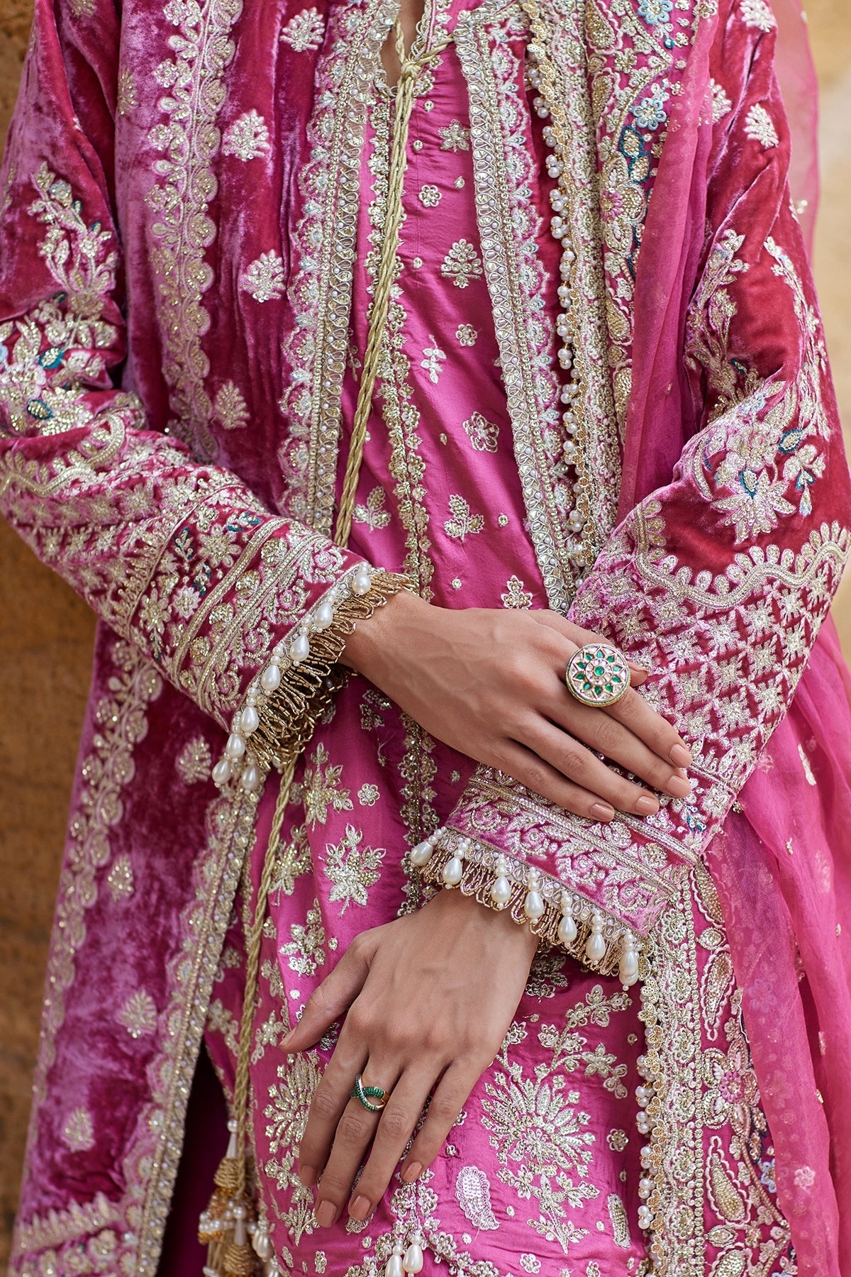 A close-up of a person wearing a rich magenta pink traditional outfit with intricate gold embroidery, silver mirror work, and a matching sheer dupatta.
