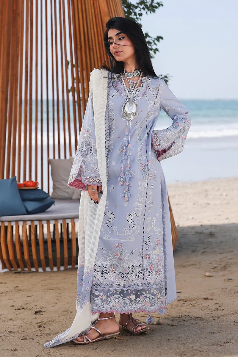 Woman in a light blue embroidered dress standing on a beach with ocean view.