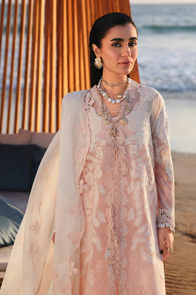 Woman in a light pink embroidered outfit standing on a beach.