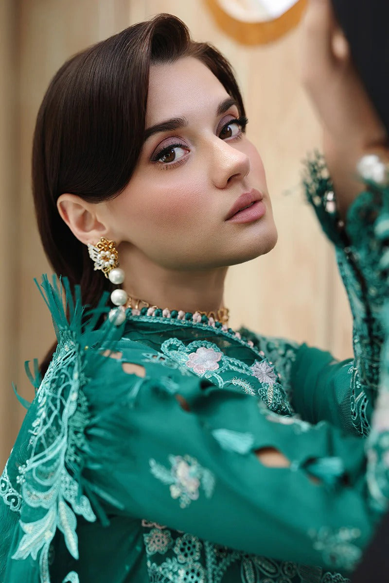 Woman in a green embroidered traditional outfit with jewelry, looking into a mirror.