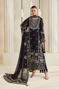A woman models a black traditional embroidered outfit with a matching sheer dupatta, featuring intricate gold and silver embroidery, tassels, and a high neckline, set against a warm beige architectural background.