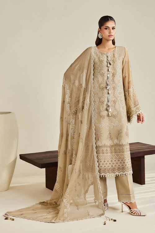A woman models a traditional beige three-piece salwar kameez suit with intricate silver embroidery, matching trousers, and a sheer dupatta, set against a minimalist beige background with a wooden bench.