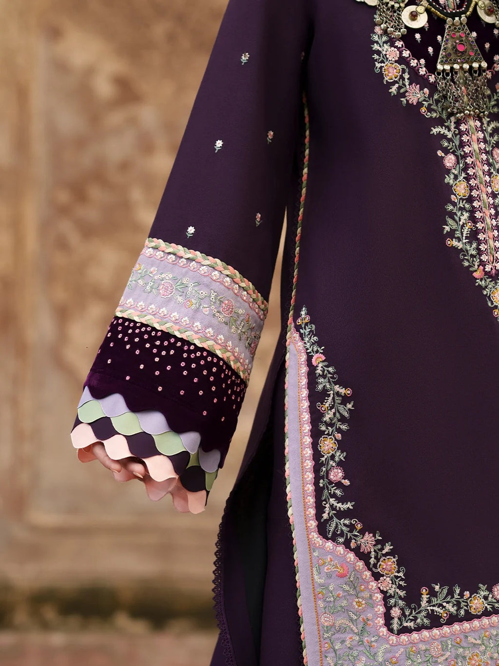 Close-up of a dark purple traditional embroidered garment with ornate floral embroidery, metallic embellishments, and a decorative multicolor scalloped cuff.