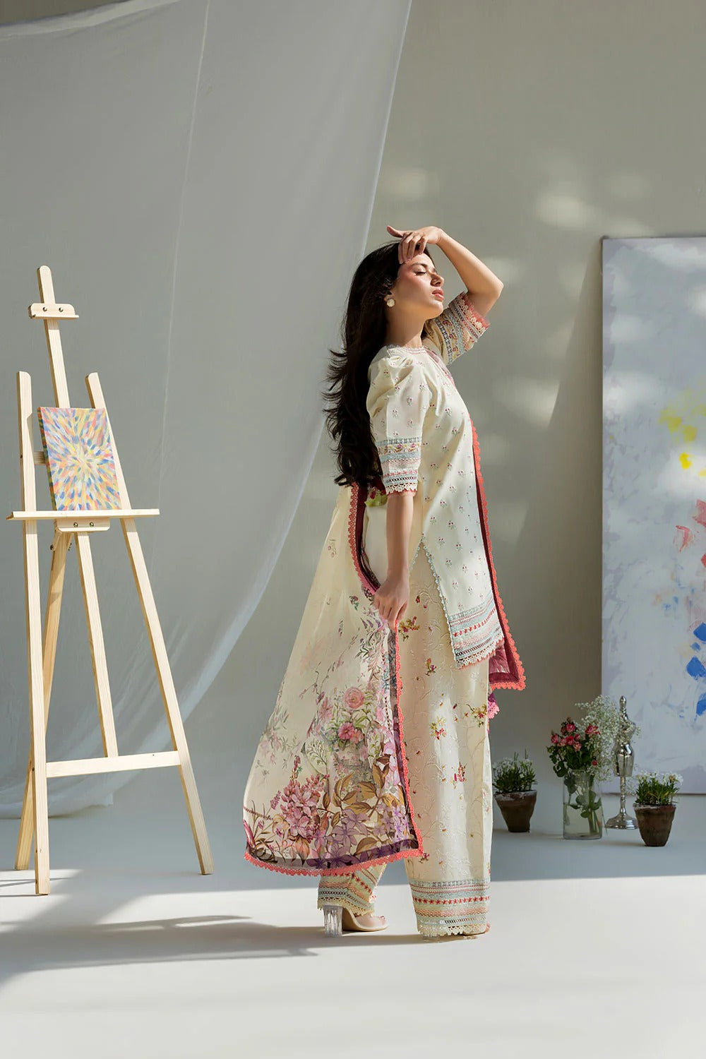 Woman in a traditional outfit standing in a studio with art easel and plants.