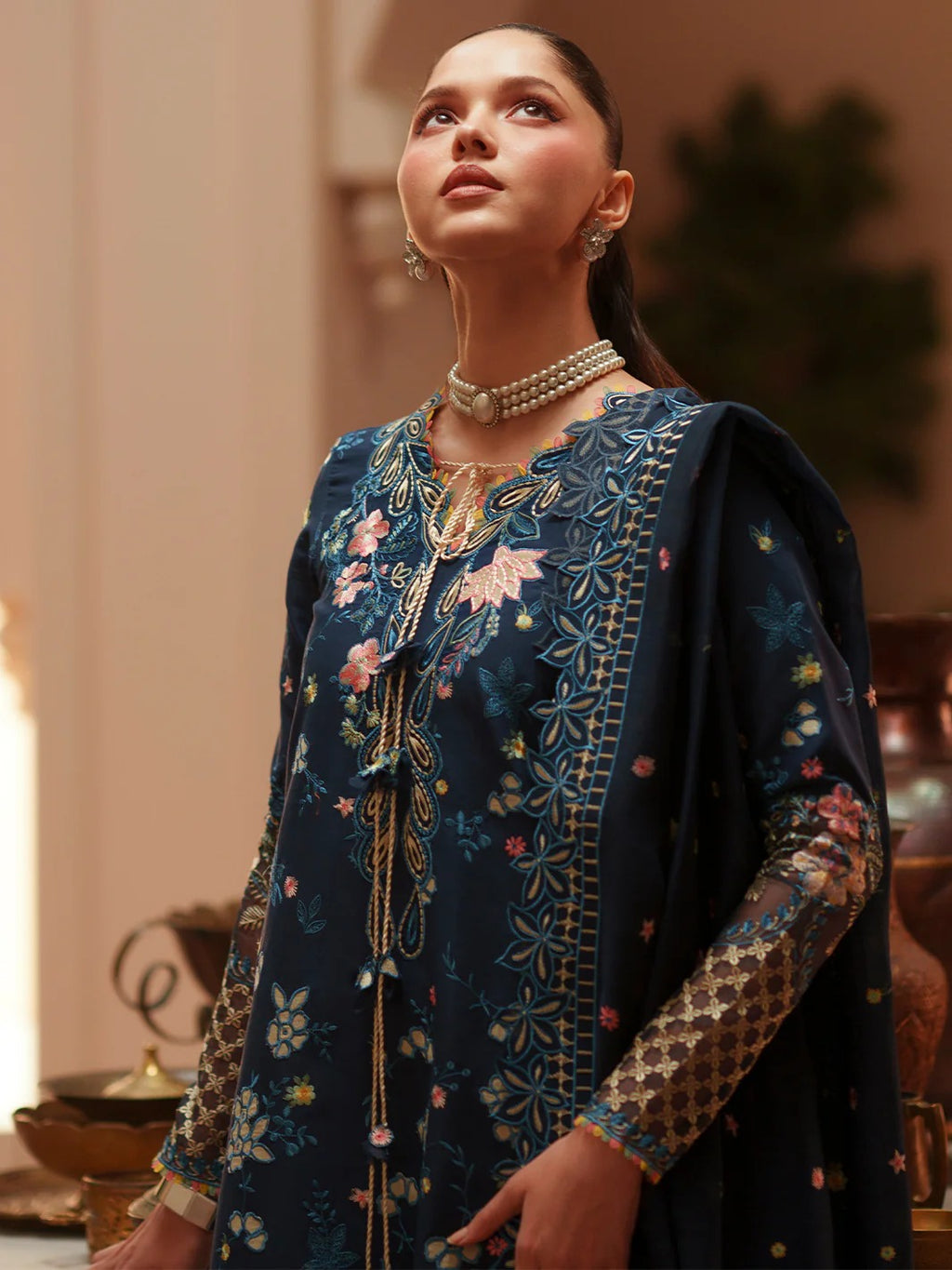 Woman wearing a dark blue embroidered traditional outfit with jewelry indoors.