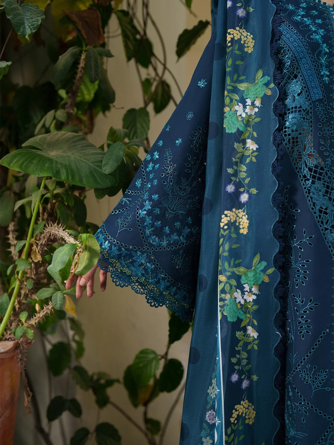 Blue embroidered fabric with floral patterns held against a plant background