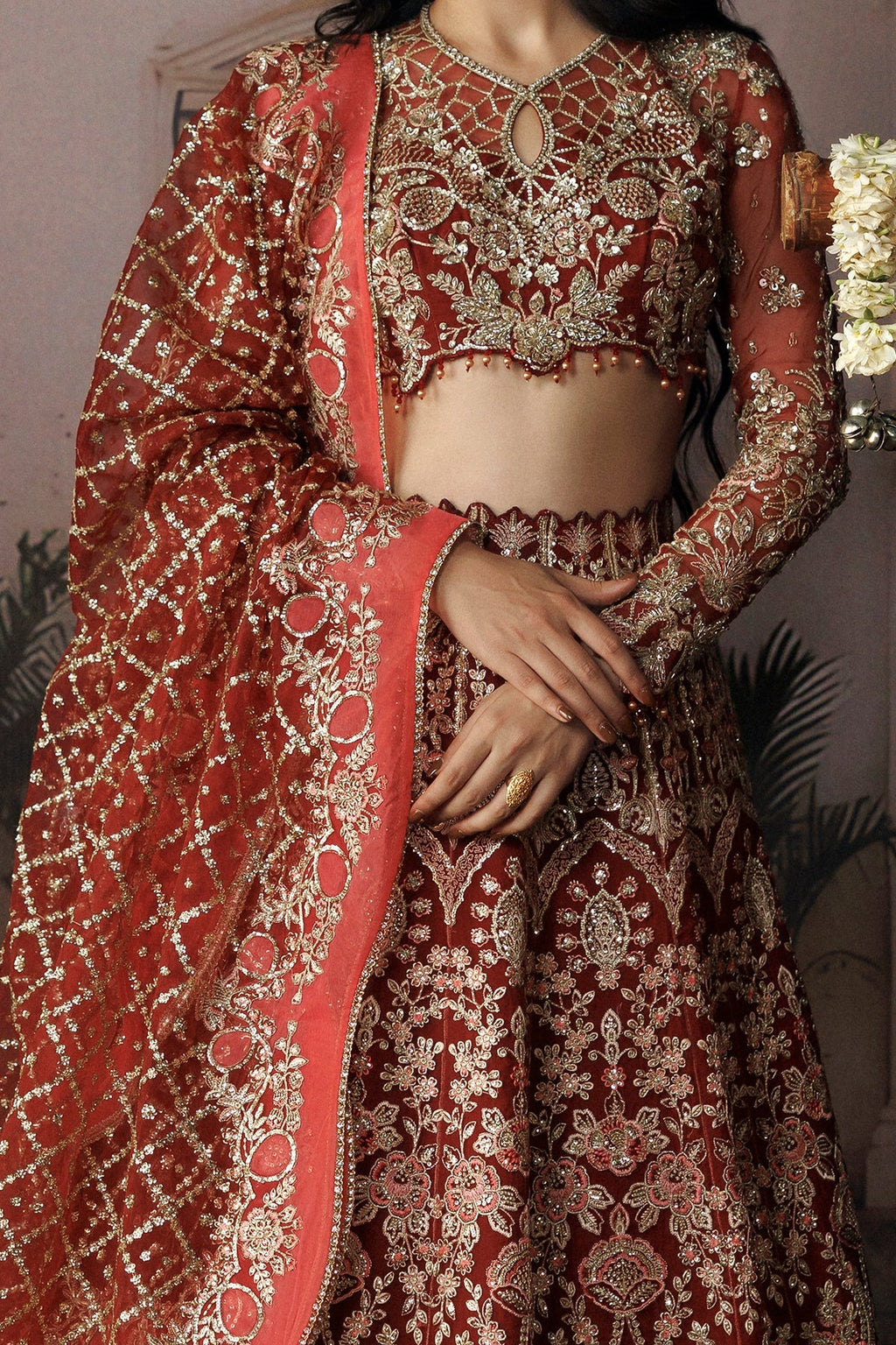 A close-up of a model wearing a traditional Indian bridal lehenga choli set in deep maroon red with intricate gold embroidery and a matching dupatta.