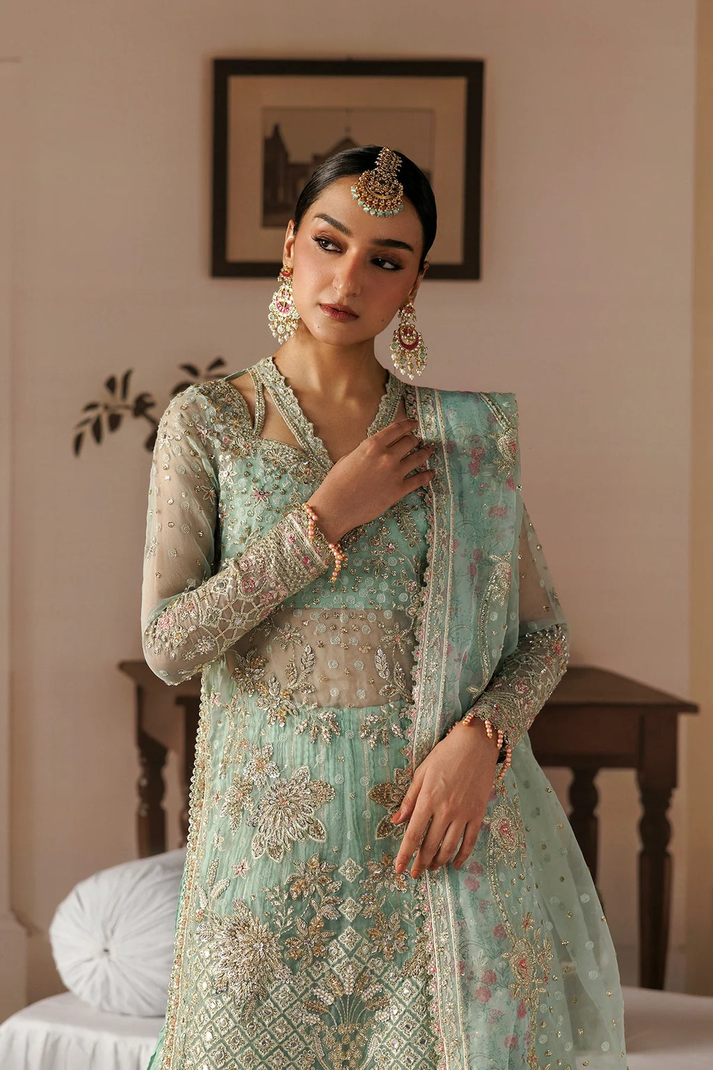 A woman models a traditional mint green and gold embroidered Indian outfit with a matching dupatta, set against a warm-toned indoor background.