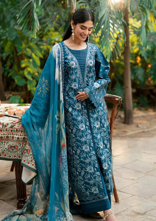 A woman wearing a traditional blue printed salwar kameez suit with a matching dupatta, standing outdoors in a garden setting.