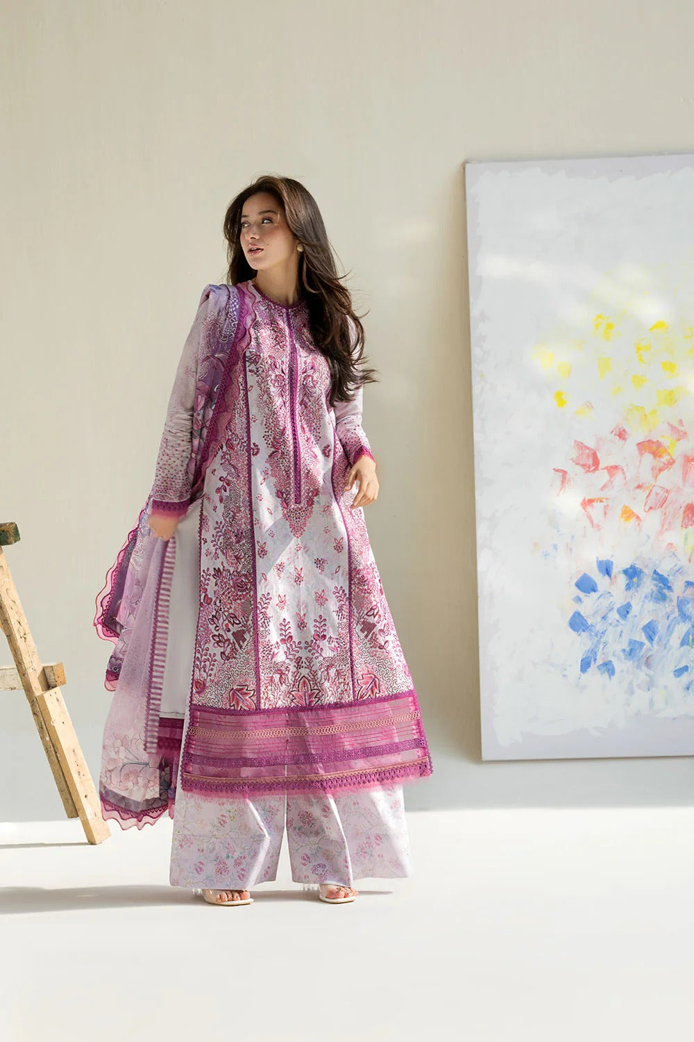 Woman in a pink and white traditional outfit standing in a room with a colorful abstract painting on the wall.