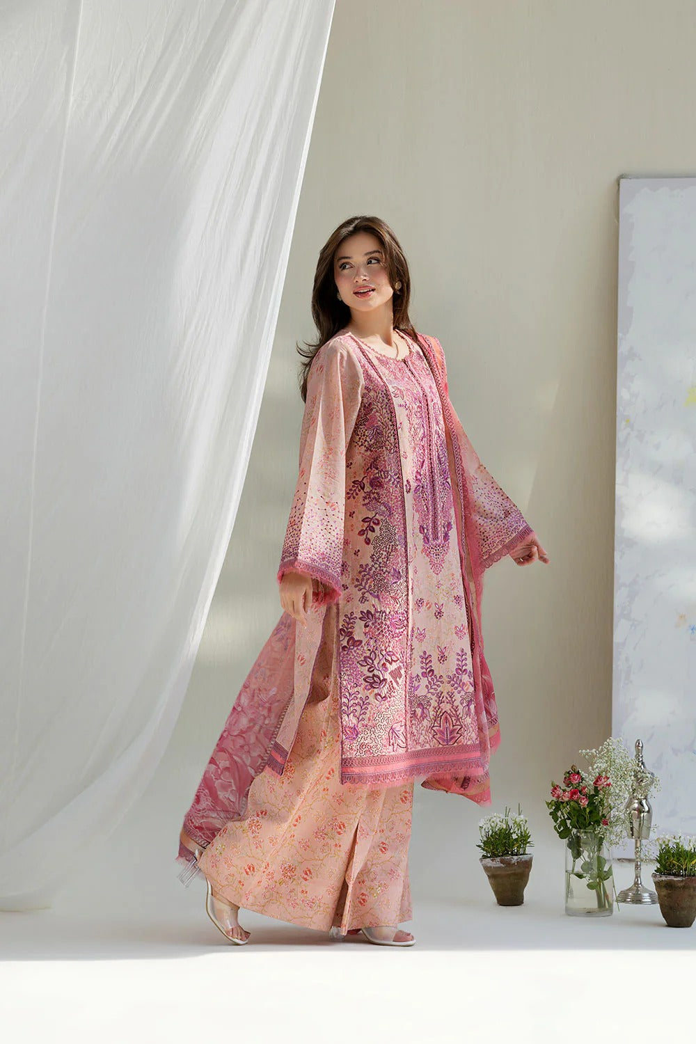 Woman wearing a pink and peach traditional outfit with a floral pattern in a minimalistic setting.