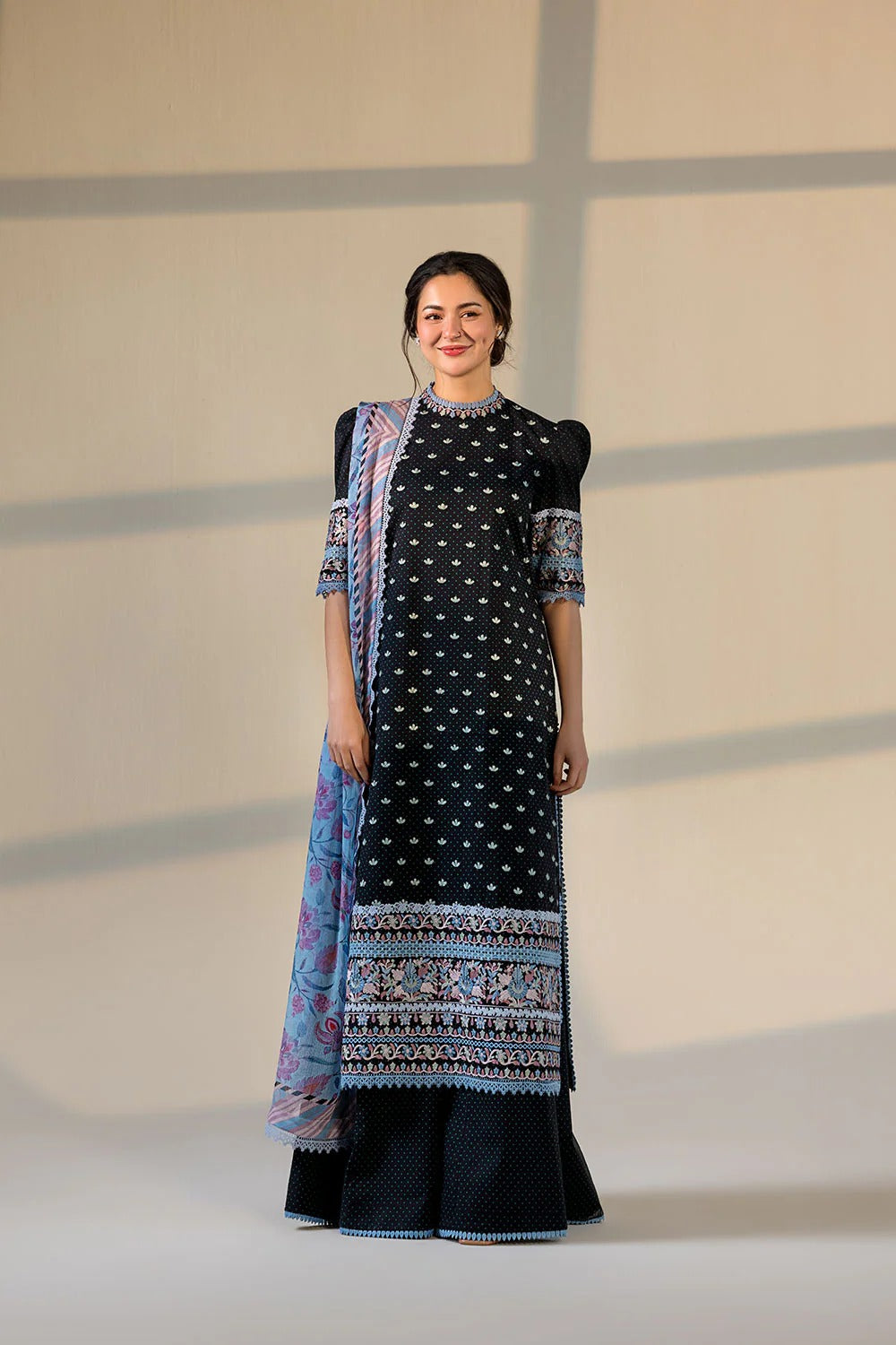 Woman wearing a black and white patterned dress with a colorful scarf against a neutral background