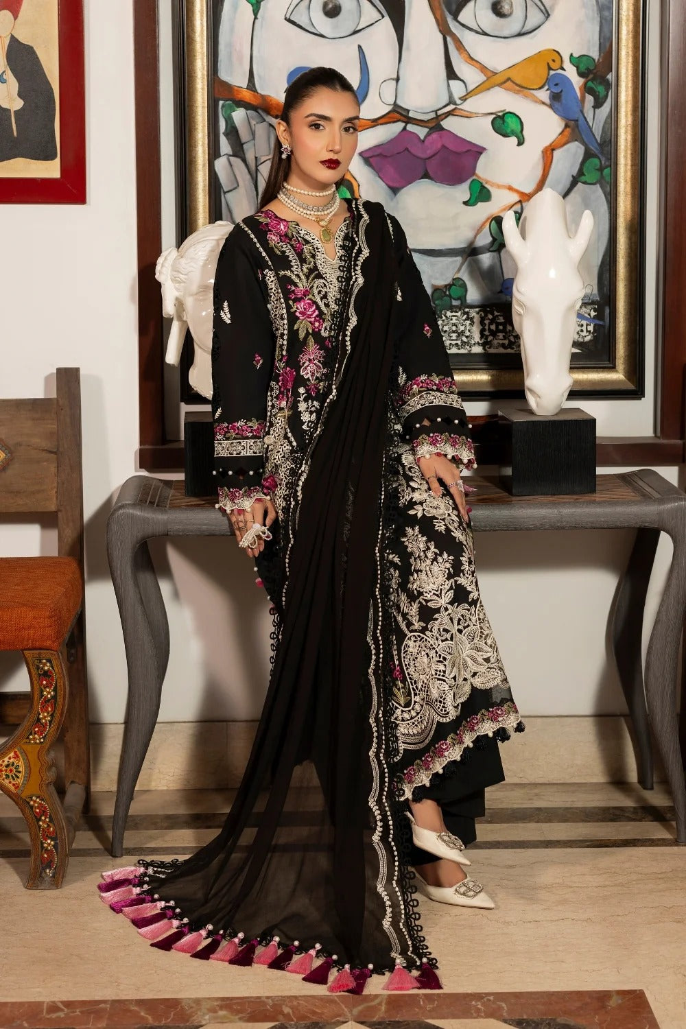 Woman in a black and white embroidered outfit standing in a room with artistic decor.