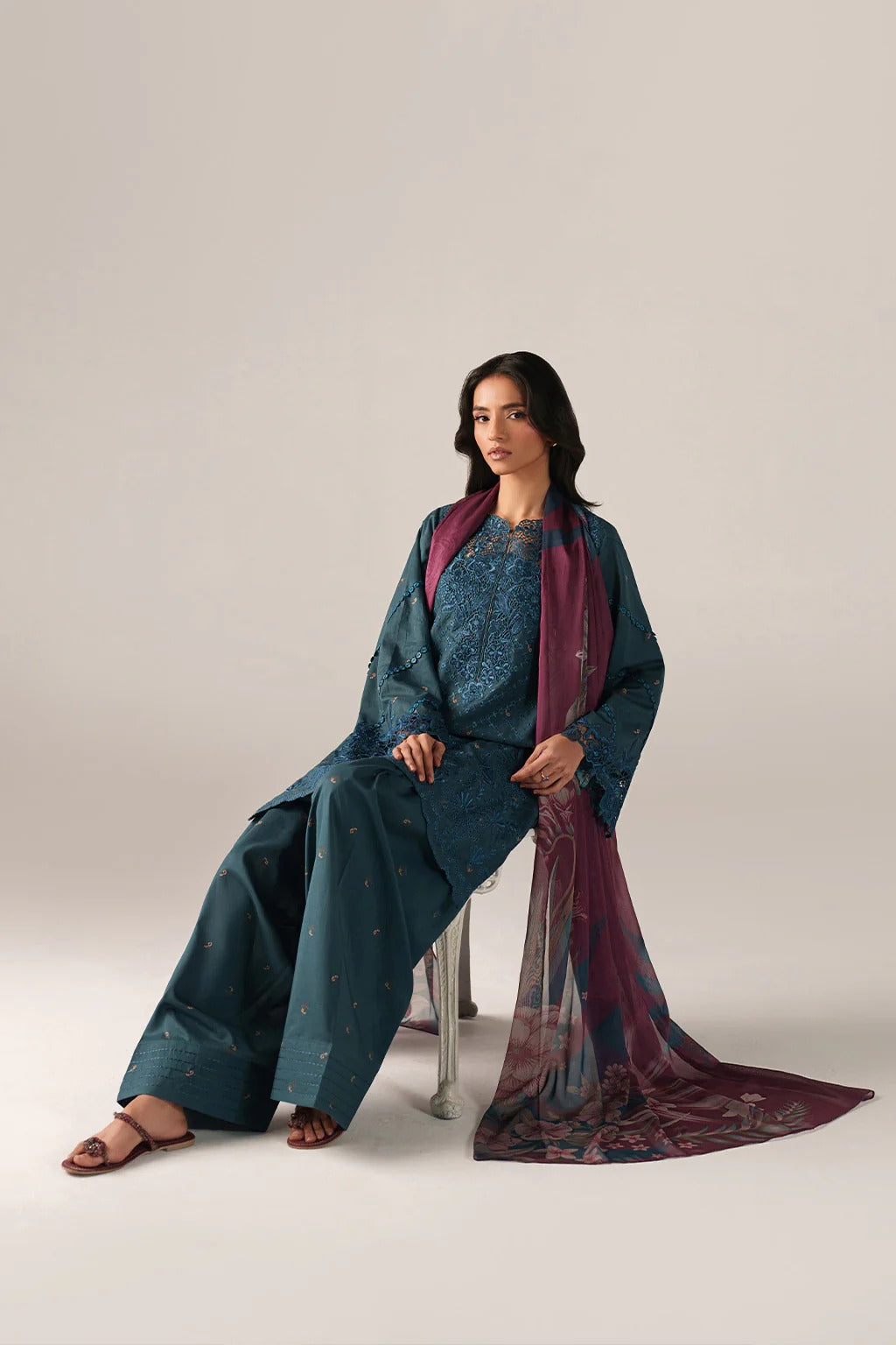 Woman wearing a teal outfit with a matching scarf on a plain background