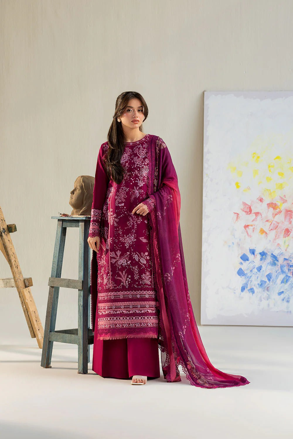 Woman in a pink traditional outfit standing in a minimalistic room with a painting on the wall.