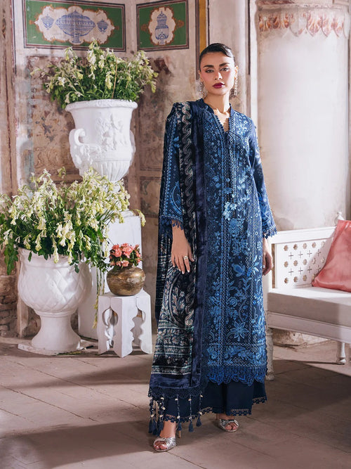 A woman models a traditional blue embroidered salwar kameez set with a matching dupatta in an ornate indoor setting with white planters and a bench.