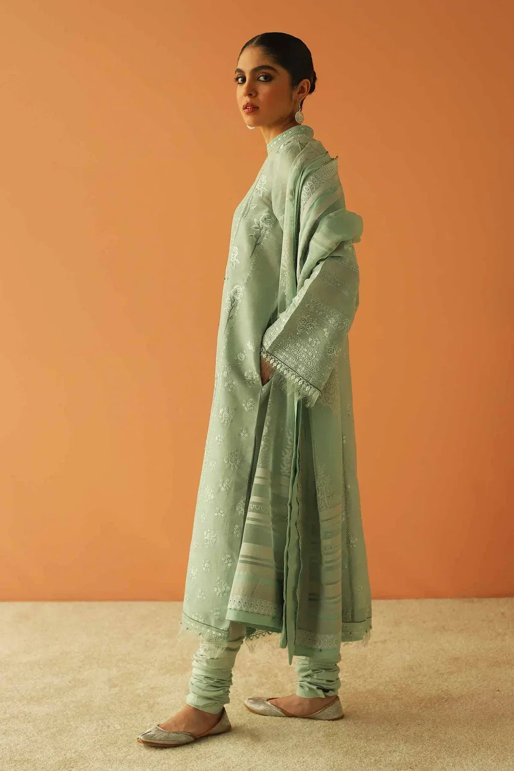 Woman wearing a light green traditional outfit against an orange background