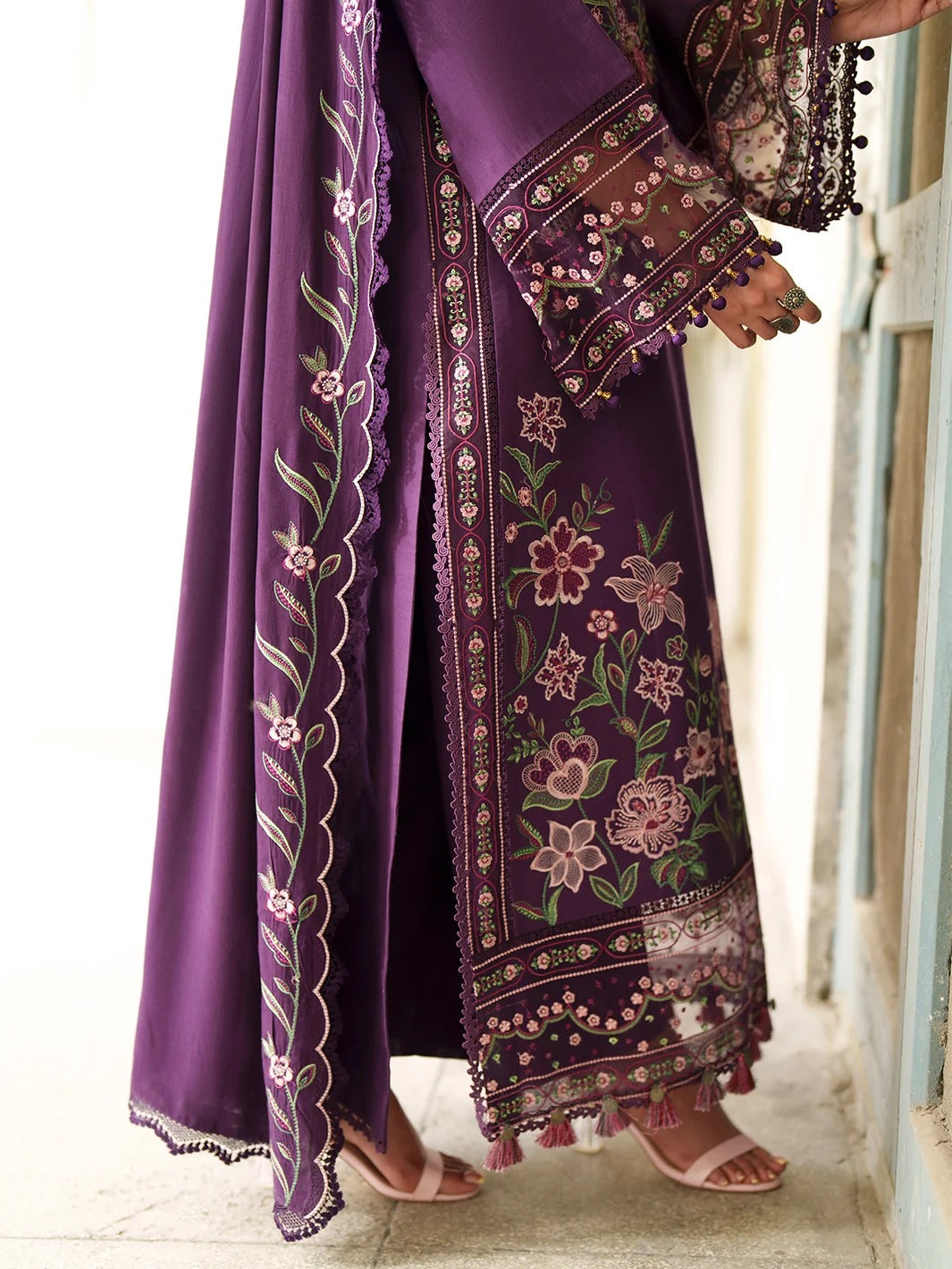 A person wearing a purple embroidered traditional outfit with a matching draped scarf, shown from the waist down in a bright indoor setting.