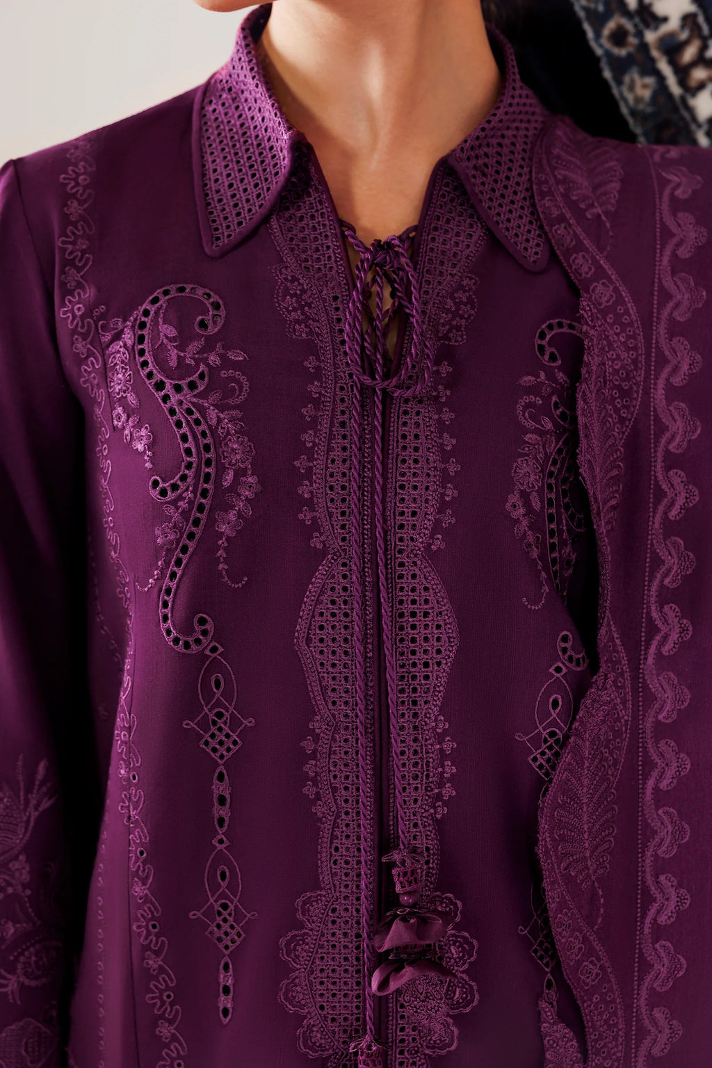 A close-up of a person wearing a deep purple embroidered blouse with intricate lace-like embroidery and a pointed collar.