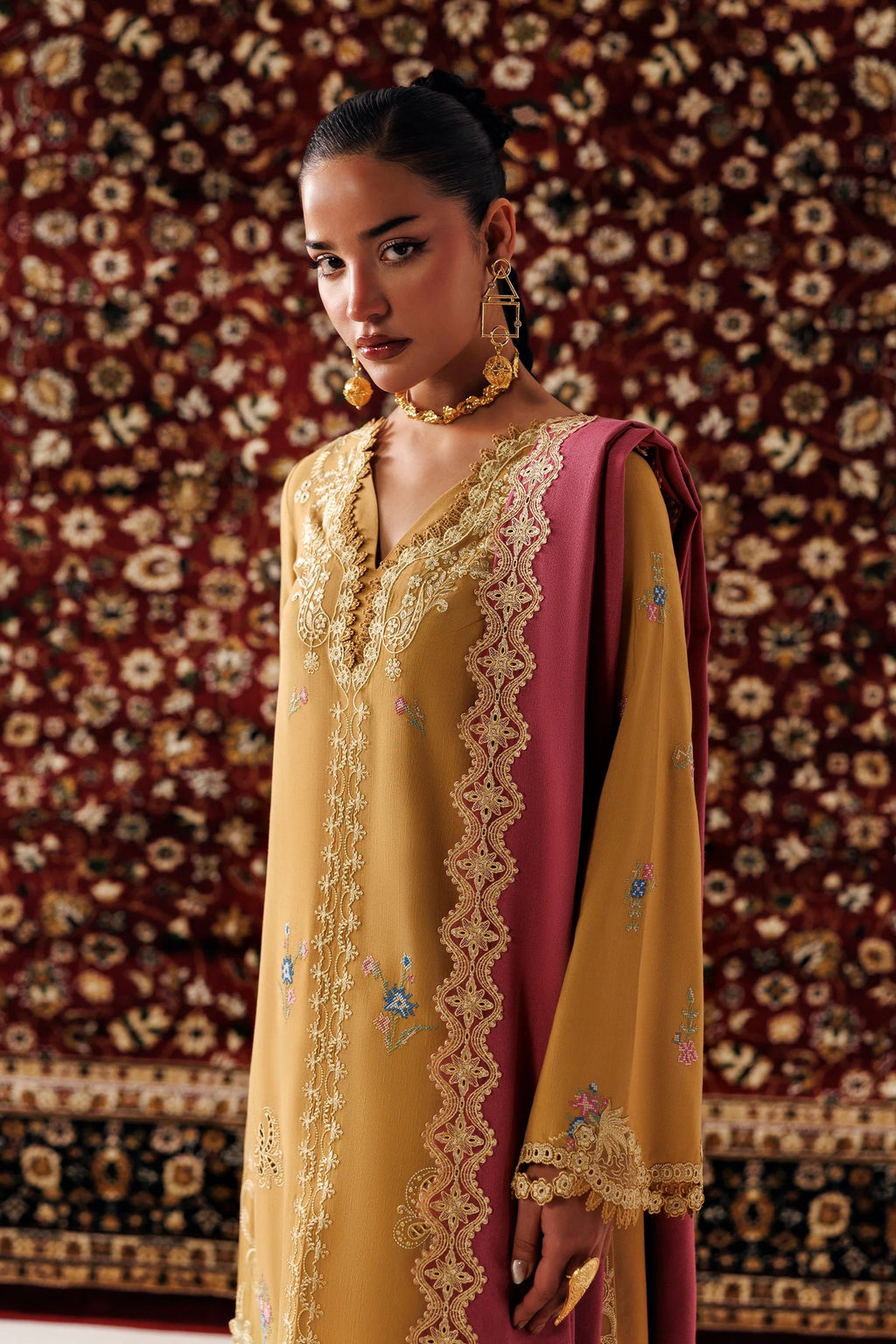 A woman models a traditional Indian salwar kameez suit. The outfit features a mustard yellow tunic with intricate gold embroidery and a deep magenta-pink dupatta draped over her shoulder.