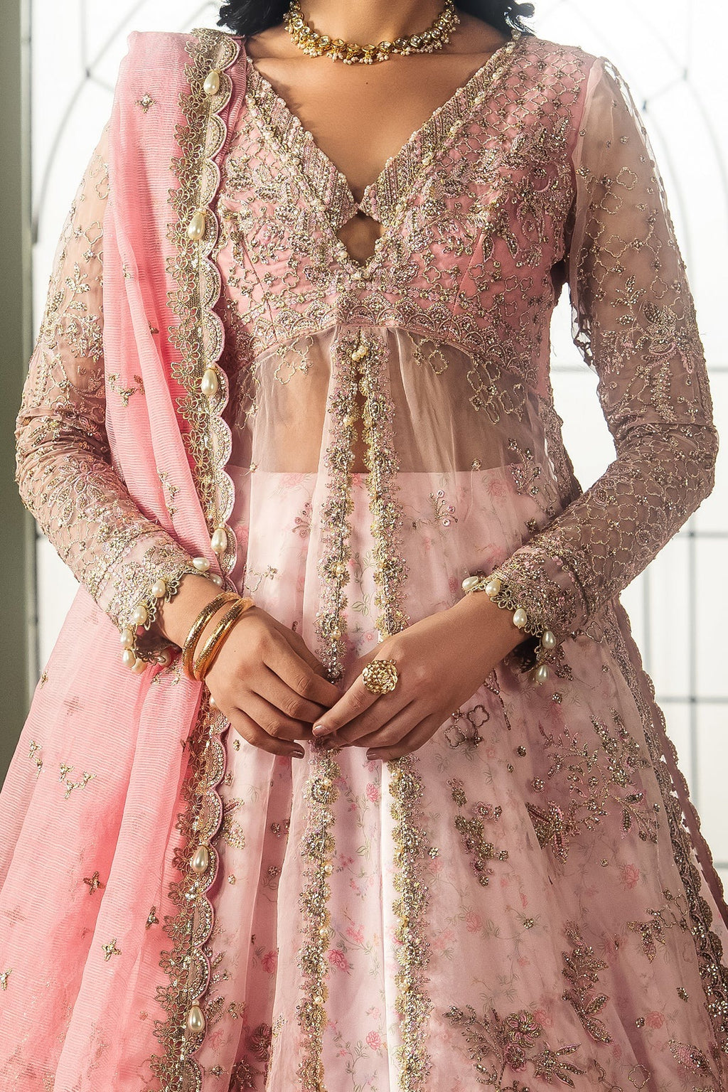 A close-up of a model wearing a pink and gold heavily-embroidered traditional Indian outfit with a matching pink dupatta.