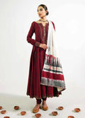 A woman models a traditional Indian outfit consisting of a long-sleeved maroon kurta with embroidered neckline, matching maroon pants, and a white dupatta with red, black, and gray patterns, set against a plain white background with small clay bowls on the floor.