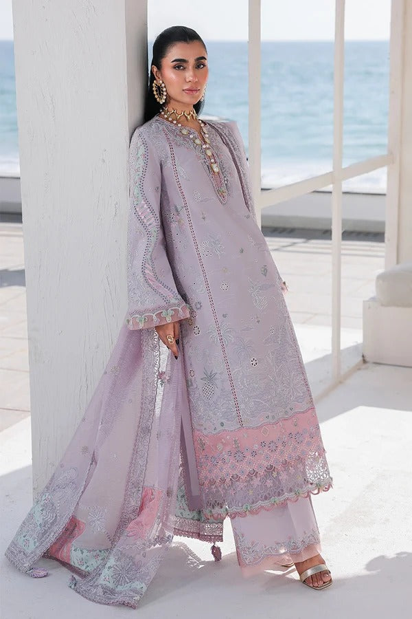 Woman in a light purple embroidered outfit standing by a white column with ocean view.
