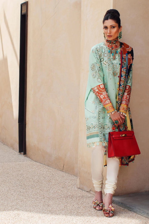 Woman in traditional outfit with a red handbag against a beige wall.