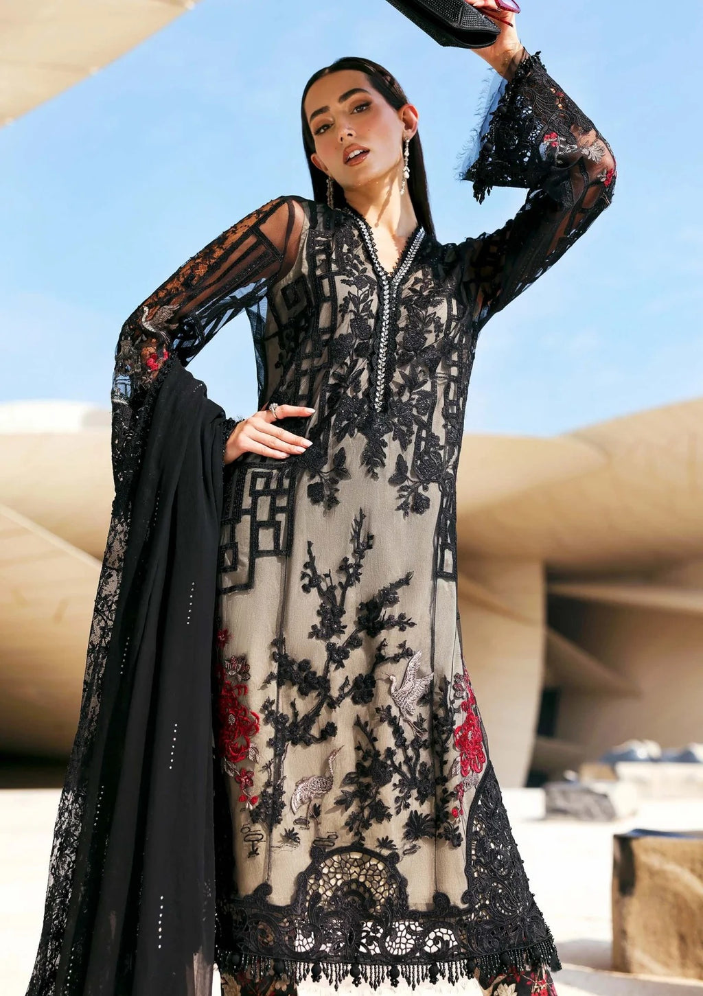 Woman wearing a black and white embroidered dress with sheer sleeves against a blue sky.